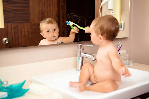 Ett litet barn med en tandborste sitter i ett handfat — Stockfoto