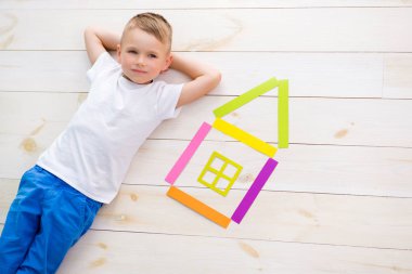 küçük çocuk renkli kağıttan bir evin yanındaki yerde yatıyor