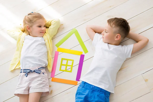 Una bambina con un ragazzo si trova sul pavimento accanto a una casa di carta colorata. Vista dall'alto — Foto Stock