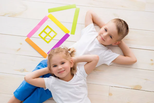 Una bambina con un ragazzo si trova sul pavimento accanto a una casa di carta colorata. Vista dall'alto — Foto Stock