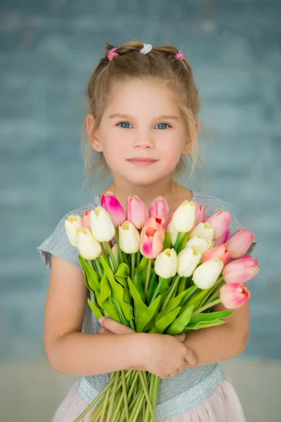 Милая улыбающаяся девочка с тюльпанами у окна — стоковое фото