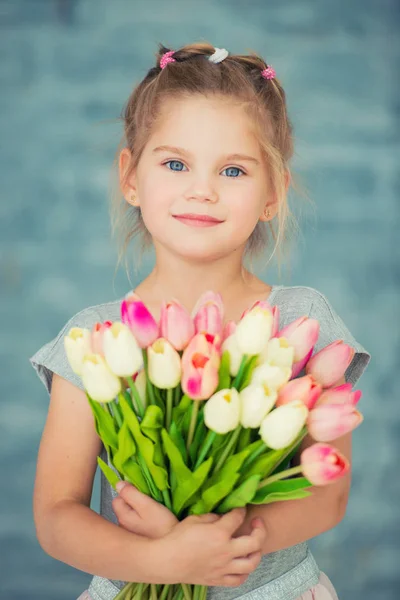 Adorable niña sonriente con tulipanes junto a la ventana — Foto de Stock