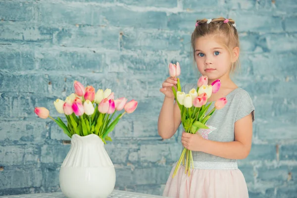 Adorable smiling little girl with tulips by the window — Stock Photo, Image