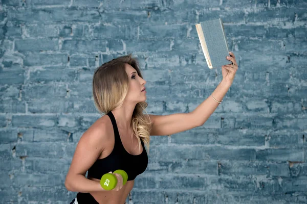 Güzel Fitness Kız Modeli Kitap Pompalar Pazı Dumbbells Okur — Stok fotoğraf