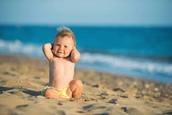 Dziecko bawi się na piasek na brzegu morza na zachód słońca — Zdjęcie stockowe