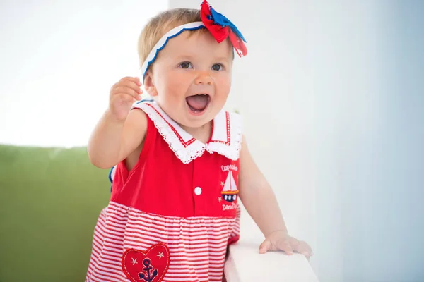 Söt liten flicka i en klänning sitter i kuddar, ler lyckligt — Stockfoto