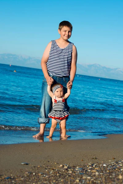 The elder brother walks with his younger sister on the beach. Walking on the beach to see the waves for the first time, family holidays.