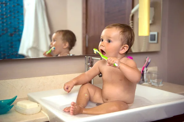 Ett litet barn med en tandborste sitter i ett handfat — Stockfoto