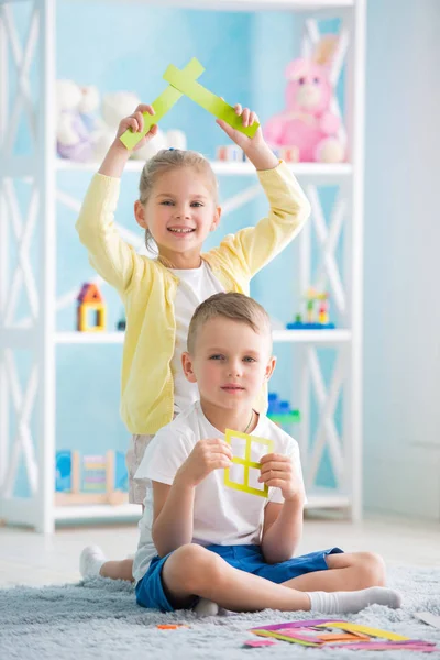 Una bambina con un ragazzo è seduta sul pavimento e tiene in mano una casa di carta colorata . — Foto Stock