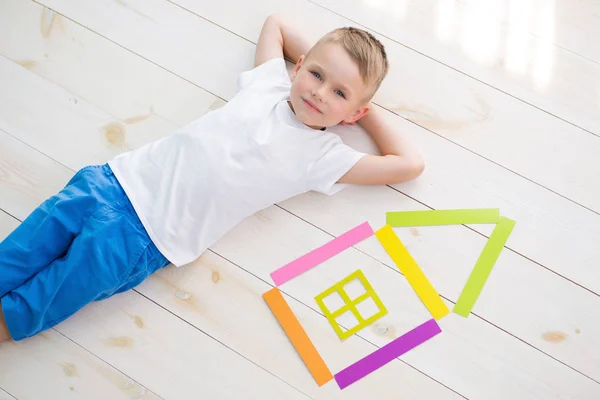 Bambino si trova sul pavimento accanto a una casa di carta colorata — Foto Stock