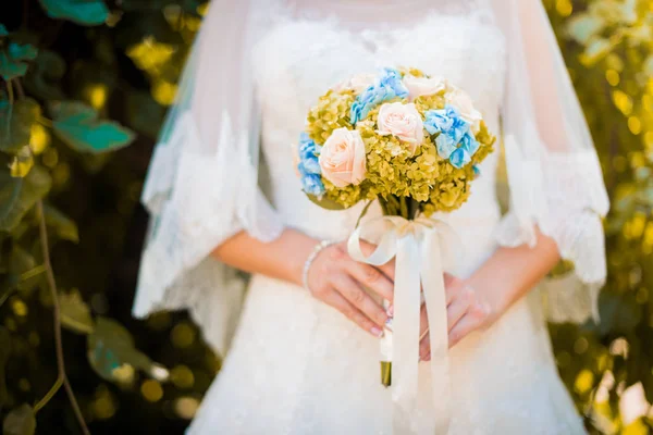 Noiva em um vestido de pé em um jardim verde e segurando um buquê de casamento de flores e vegetação. — Fotografia de Stock