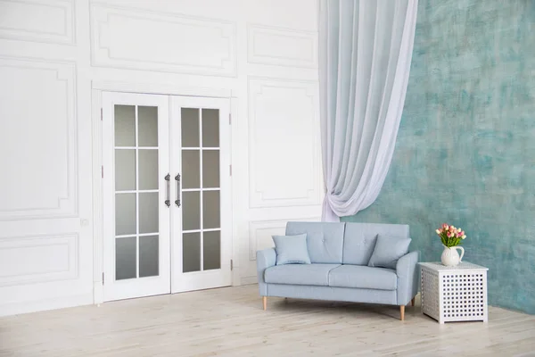 Chambre blanche est un canapé bleu, un piédestal avec des fleurs dans un vase . — Photo