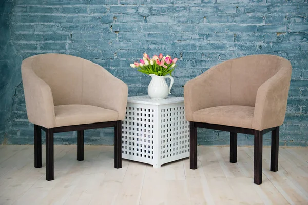 Deux fauteuils gris, une table et des fleurs contre un mur de briques gris. Intérieur — Photo