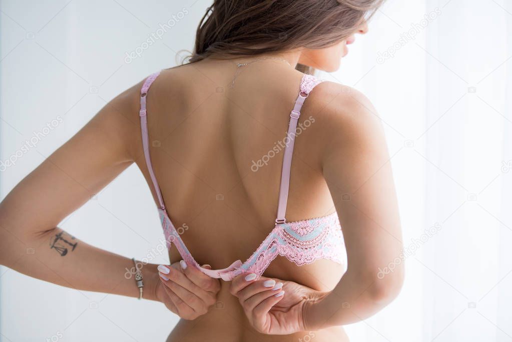 Young brunette woman unzips her back bra.