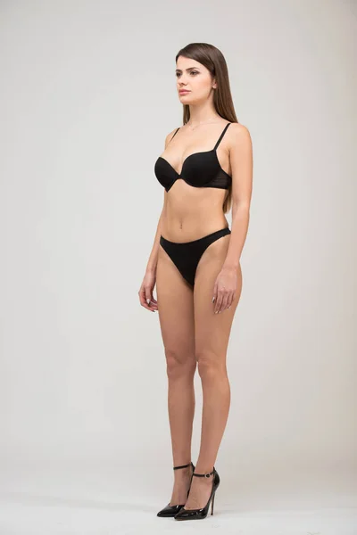 Full length portrait three-quarter of beautiful brunette women with slim figure in black bra and shorts. Model snaps in the studio on white background.