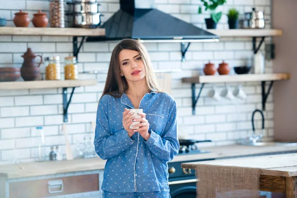 Portrait of a beautiful young girl with a cup of tea or coffee in blue pajamas in the kitchen. Early morning rise - is apledge of energy and health — Stock Photo, Image