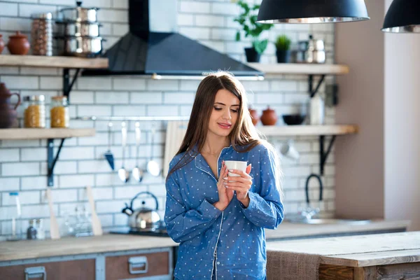 Portrait of a beautiful young girl with a cup of tea or coffee in blue pajamas in the kitchen. Early morning rise - is apledge of energy and health — Stock Photo, Image