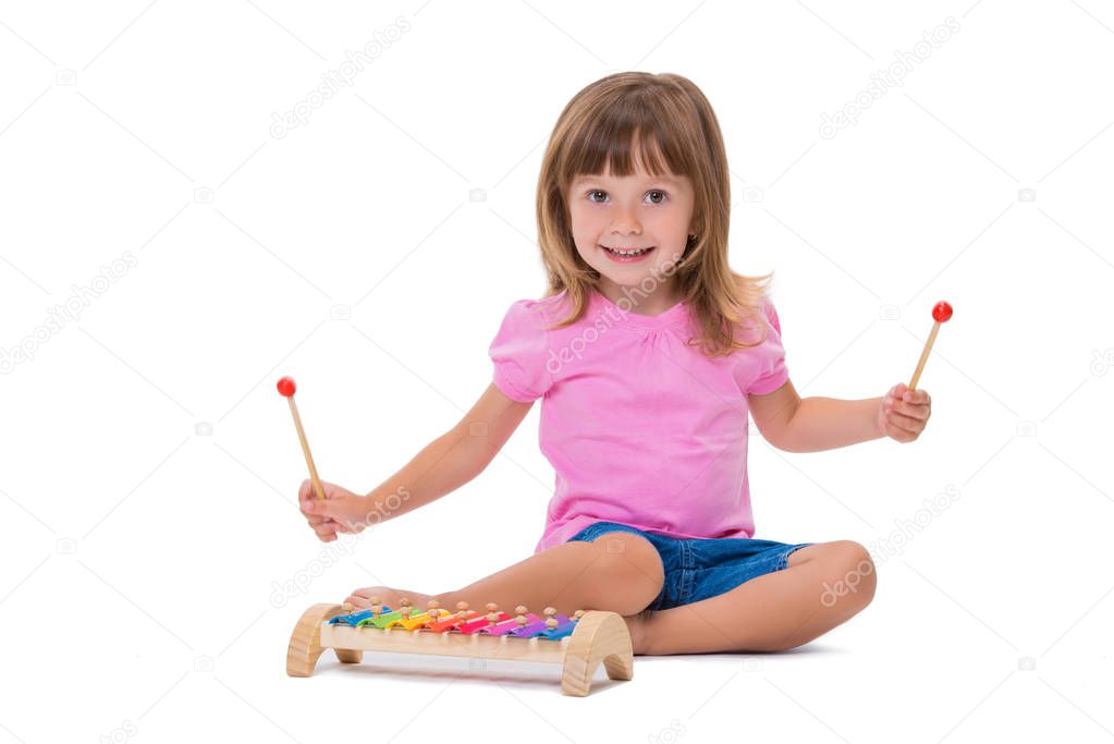 Cute smiling cheerful positive girl 3 years old playing with musical instrument toy xylophone isolated on white background.