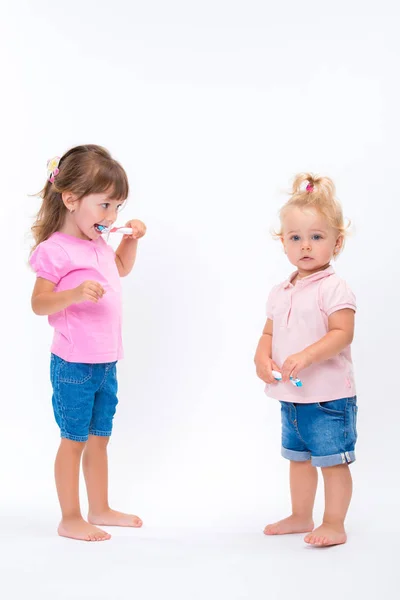 两个女孩姐妹在粉红色的 T恤与牙刷站立到他们的充分的高度查出在白色背景 儿童口腔和口腔卫生 — 图库照片