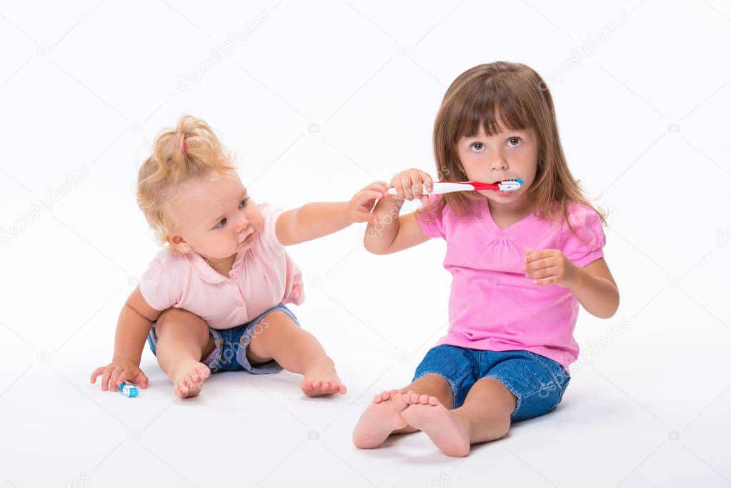Two girls sisters in pink t-shirt with toothbrushes stand to their full height isolated on white background. Children oral and dental hygiene.