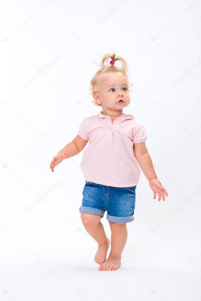 Cute little child baby girl learns to walk, make first steps isolated on a white background.