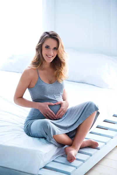 Piękna Ciąży Młoda Kobieta Siedzi Łóżku Pokoju Sprawia Serce Jej — Zdjęcie stockowe