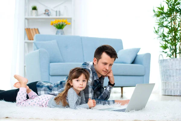 かわいい小さな女の子 若いお父さん父や兄弟を見て居間の床のカーペットの上に横たわって パソコン モニター — ストック写真