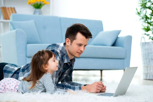 かわいい小さな女の子 若いお父さん父や兄弟を見て居間の床のカーペットの上に横たわって パソコン モニター — ストック写真