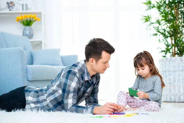 父亲和小女儿有优质的家庭时间在家里 爸爸与女孩躺在温暖的地板上画与五颜六色的毛毡提示铅笔 — 图库照片