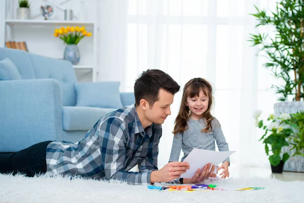 父と娘の質家族の時間は家で一緒に楽しんで カラフルで暖かい床に横たわった少女とお父さんを感じたヒント鉛筆 — ストック写真