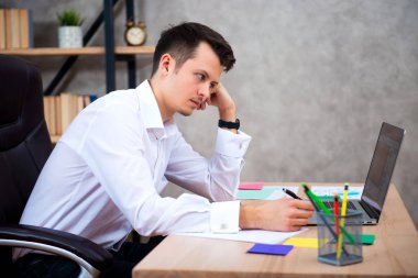 Dizüstü bilgisayarda çalışarak ve mali bir problem çözme hakkında düşünme ofis masasında oturan genç Yöneticisi adam konsantre.