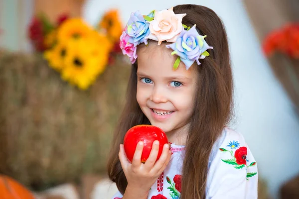 Sorrindo menina loira com cabelos longos em uma grinalda ucraniana colorida e em bordado está sentado em palheiros. Decoração de outono, colheita com abóboras — Fotografia de Stock