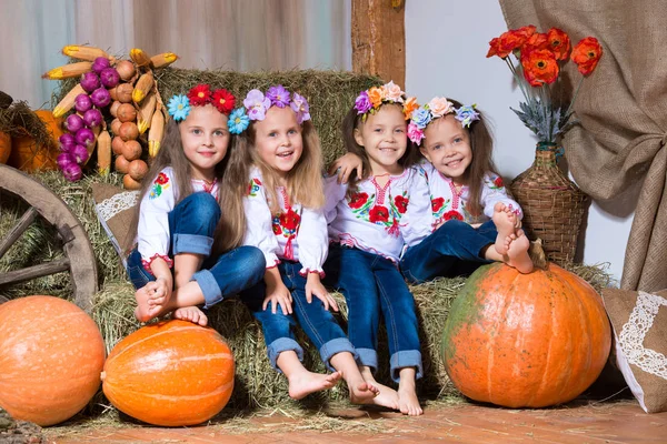 Čtyři usmívající se dívky dvojčata v ukrajinských věnce sedět na stohy. Podzimní výzdoba, sklizeň s dýně — Stock fotografie