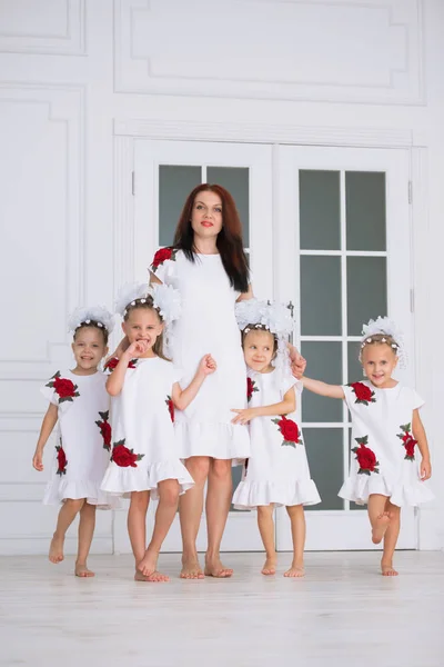 Счастливая многодетная семья матери с четырьмя дочерьми в вышитых белых платьях напротив двери в интерьер — стоковое фото