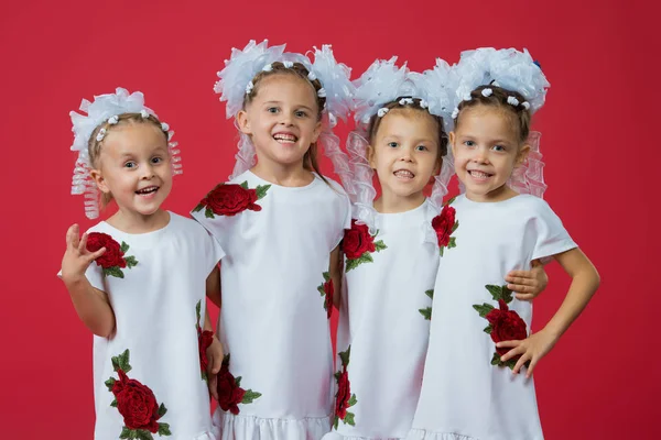 Glückliche große Familie von vier Schwestern in bestickten weißen Kleidern auf schlichtem roten Hintergrund im Atelier — Stockfoto