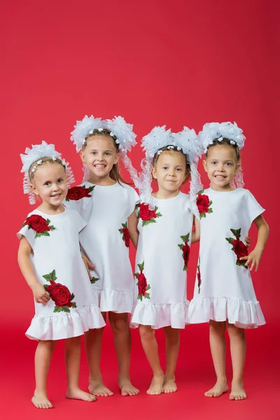 Feliz gran familia de cuatro hermanas en vestidos blancos bordados sobre un fondo rojo liso en el estudio —  Fotos de Stock