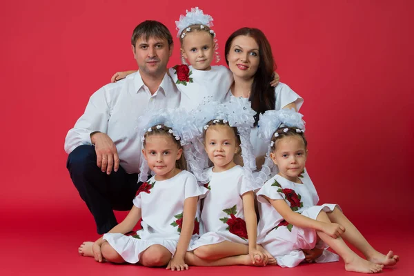 Большая счастливая семья: родители - отец, мать и дети - близнецы в вышитых платьях с орнаментом на красном фоне в студии — стоковое фото
