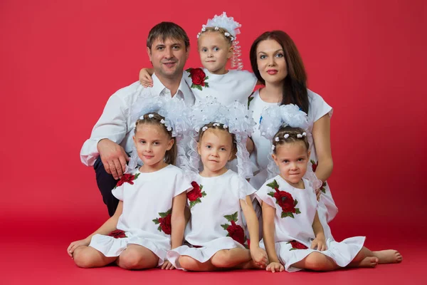Большая счастливая семья: родители - отец, мать и дети - близнецы в вышитых платьях с орнаментом на красном фоне в студии — стоковое фото
