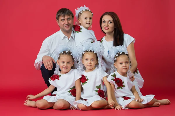Велика щаслива сім'я: батьки батько, мати і діти близнюки у вишитих сукнях з орнаментом на червоному тлі в студії — стокове фото