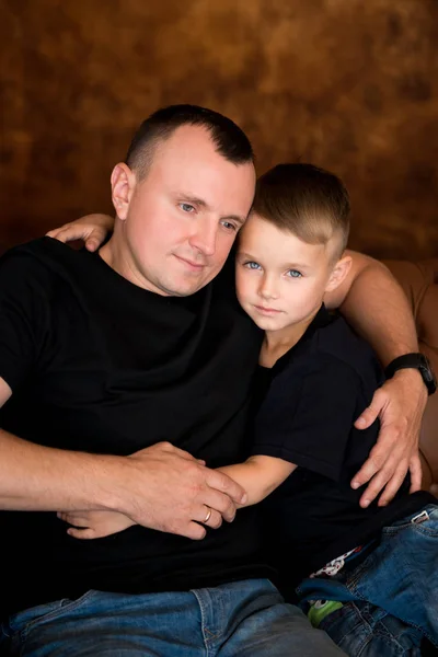 Otec drží malého syna. Detailní záběr na rodinný portrét na hnědé pozadí. Rodinné lásky a šťastné otcovství — Stock fotografie