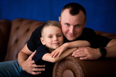 Baba ve küçük oğlu deri kanepeye, gülümseyen ve Birbirinizle konuşmak oturuyor. Mutlu babalık ve aile sevgisi. Aile portresi
