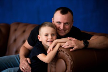 Baba ve küçük oğlu deri kanepeye, gülümseyen ve Birbirinizle konuşmak oturuyor. Mutlu babalık ve aile sevgisi. Aile portresi