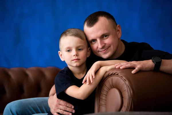 Padre e hijo pequeño están sentados en un sofá de cuero, sonriendo y hablando entre sí. Feliz paternidad y amor familiar. Retrato familiar — Foto de Stock