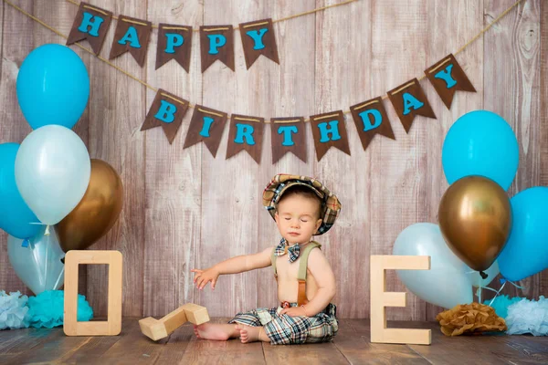 Feliz aniversário, cavalheiro. O menino está vestido com um traje retro com suspensórios, um boné e um laço e senta-se entre os balões. Criança 1 ano — Fotografia de Stock