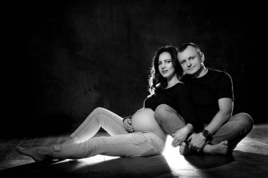 Güzel hamile çift kadın ve erkek bir koyu siyah arka plan üzerine poz. Aile sevgisi ve bebek beklentisi