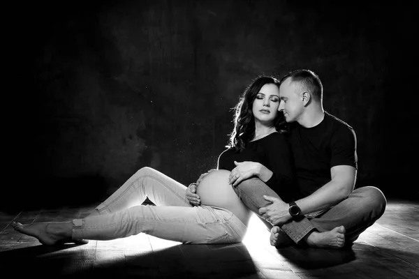 Красивая беременная пара женщина и мужчина позируют на тёмном чёрном фоне. Семейная любовь и ожидание ребенка — стоковое фото