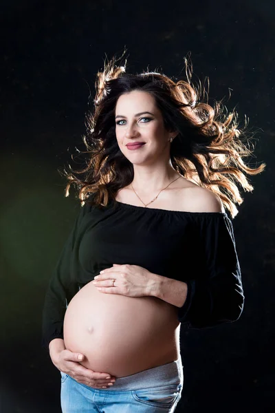 Bellissima maternita '. Sottile donna incinta con i capelli che volano nel vento su uno sfondo nero. Felice gravidanza e maternità sana — Foto Stock