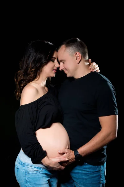 Bonito casal grávida mulher e homem uma posando no fundo preto escuro. Amor familiar e expectativa do bebê — Fotografia de Stock