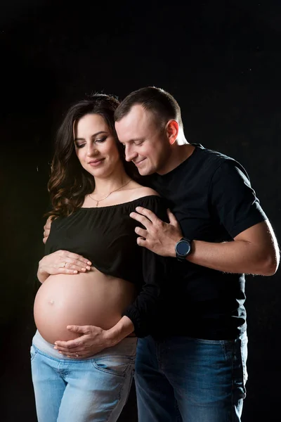 Bonito casal grávida mulher e homem uma posando no fundo preto escuro. Amor familiar e expectativa do bebê — Fotografia de Stock