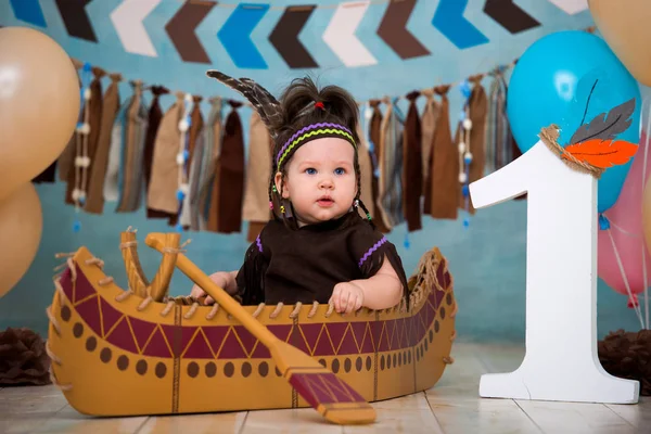 小可爱的女孩在阿帕奇印度酋长的服装和羽毛头饰坐在独木舟。儿童假期第一个生日和粉碎蛋糕1年 — 图库照片